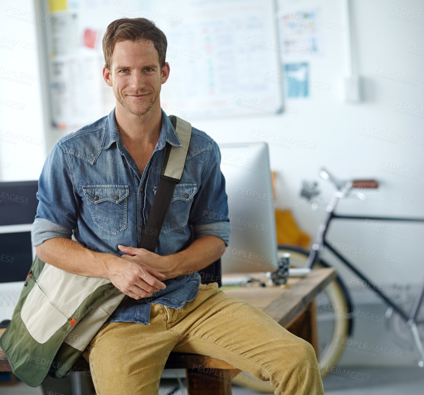 Buy stock photo A handsome young man with a satchel bag sitting on his desk
