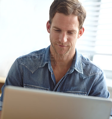 Buy stock photo A handsome young man working on his laptop in the office