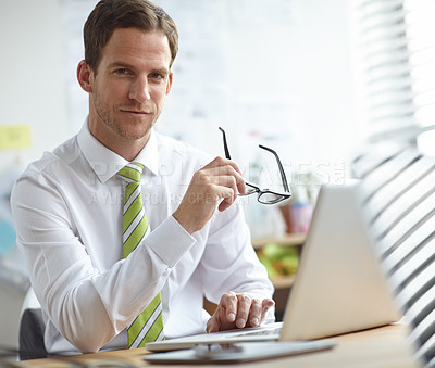 Buy stock photo A handsome young businessman sitting at his desk while looking at the camera