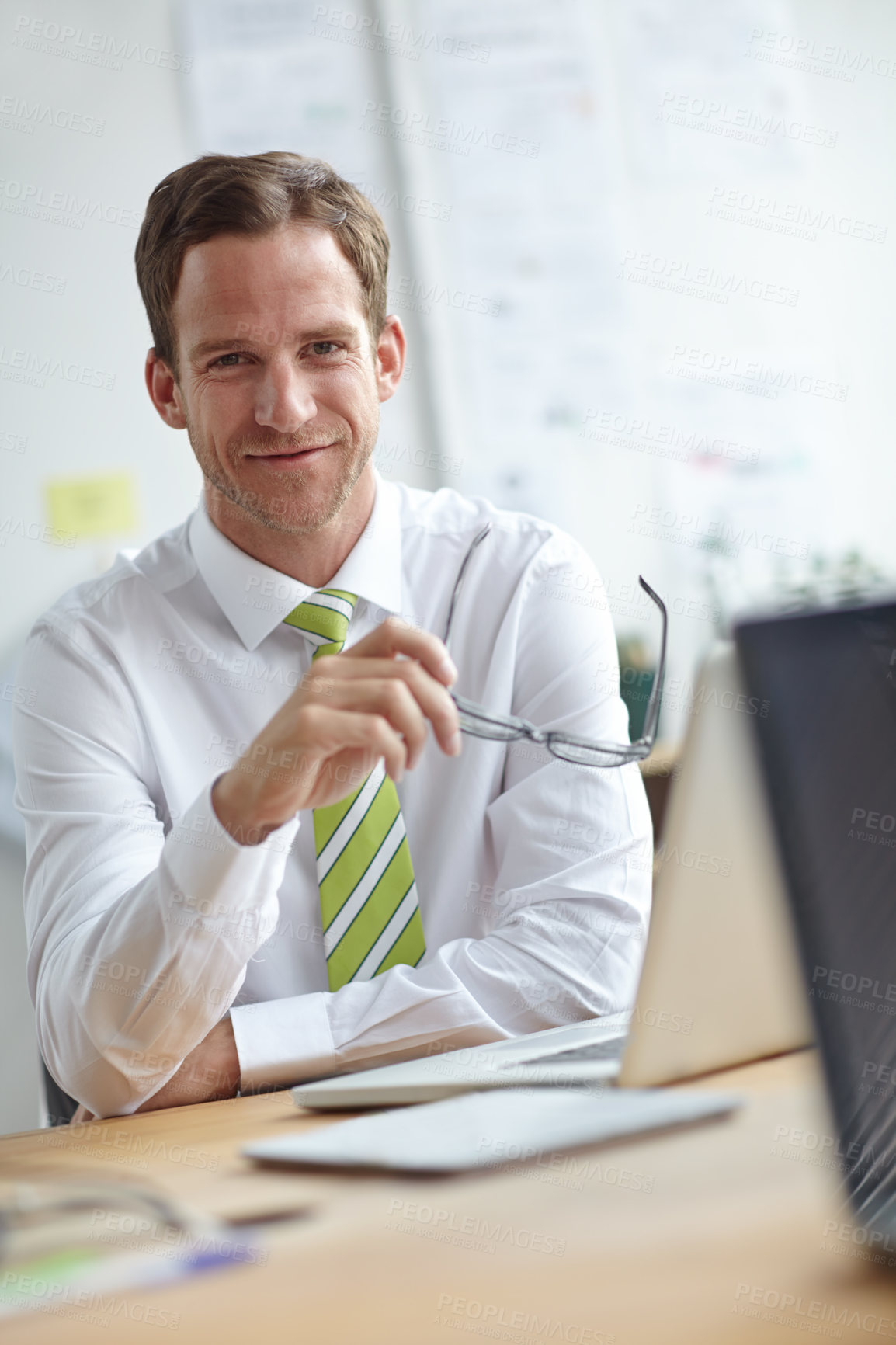 Buy stock photo A handsome young businessman sitting at his desk while looking at the camera