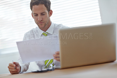 Buy stock photo A young businessman looking at a document while sitting in his office