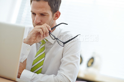 Buy stock photo A young businessman looking pensively at his laptop