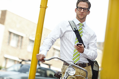Buy stock photo A young businessman standing with his bicycle while sending a text message