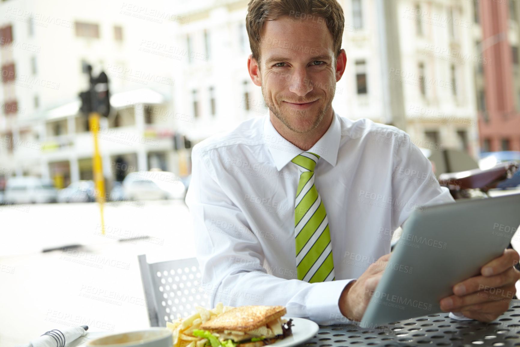 Buy stock photo A young businessman working on his digital tablet while sitting at an outdoor cafe