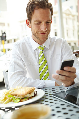 Buy stock photo A young businessman sending a text message while sitting at an outdoor cafe