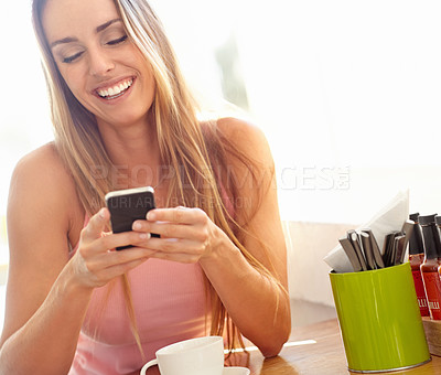 Buy stock photo A beautiful young woman sitting in a coffeeshop smiling as she reads a text message 