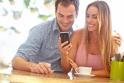Buy stock photo A happy young couple sitting in a coffee shop reading a text message and smiling
