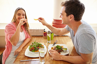 Buy stock photo A beautiful young wman laughing while her boyfriend offers her a taste of his food in a restaurant