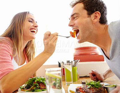 Buy stock photo A happy young woman offering her boyfriend a bite of her food in a restaurant