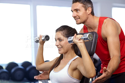 Buy stock photo A trainer helping a young woman with her weight-training at the gym