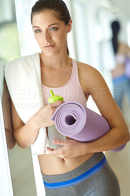 Buy stock photo A gorgeous young woman standing at the gym holding an exercise mat and a bottle of water