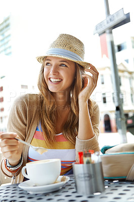 Buy stock photo A young woman stirring her cappucino while sitting at a sidewalk cafe in the city
