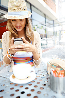 Buy stock photo A casual young woman sending a text message while sitting at a sidewalk cafe in the city
