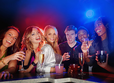 Buy stock photo A multi-ethnic group of young friends smiling at the camera while they enjoy drinks in a nightclub