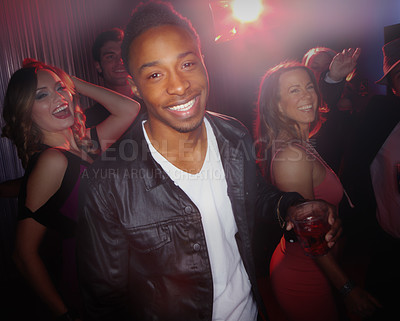 Buy stock photo A handsome young African-American man smiling at the camera while standing on the dancefloor with beautiful women dancing in the background