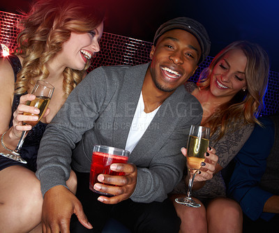 Buy stock photo A handsome young African-American man sitting in a nightclub with two beautiful caucasian women next to him