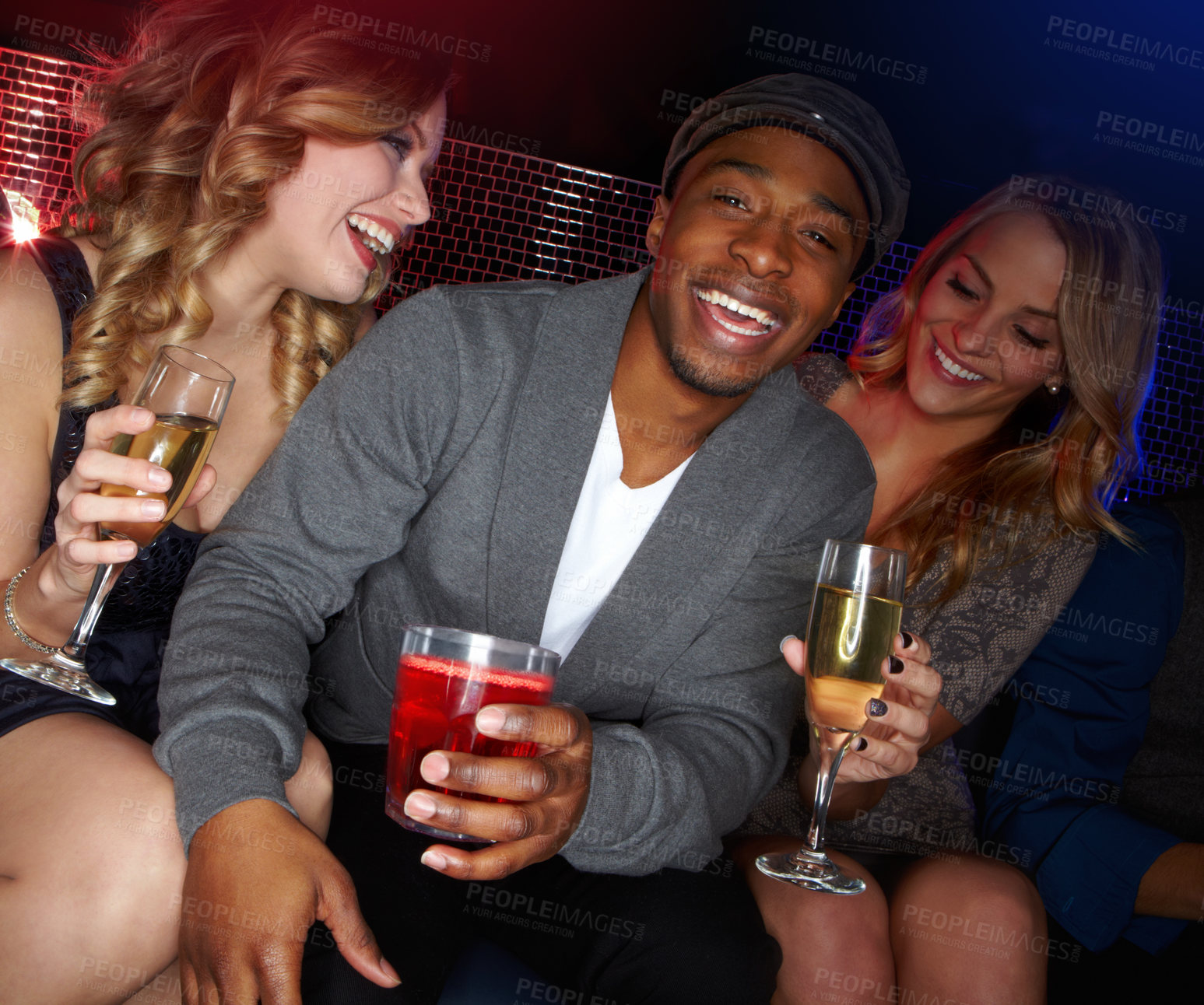 Buy stock photo A handsome young African-American man sitting in a nightclub with two beautiful caucasian women next to him