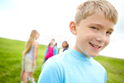 Buy stock photo Cute little boy smiling while standing outdoors with some friends in the background