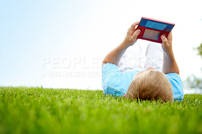Buy stock photo A little boy playing on a nintendo gaming console while lying on the grass outdoors