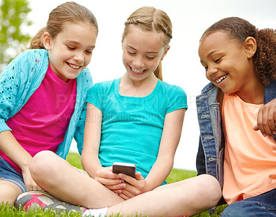 Buy stock photo Three little girls spending time together and sharing a smartphone while outdoors
