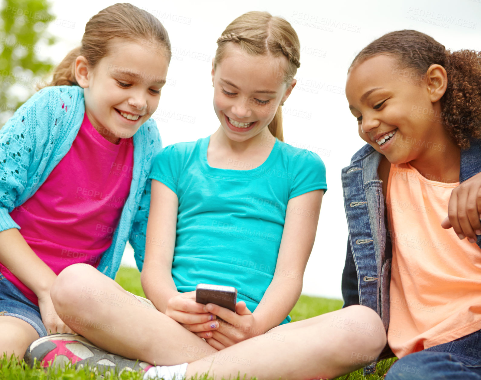 Buy stock photo Three little girls spending time together and sharing a smartphone while outdoors