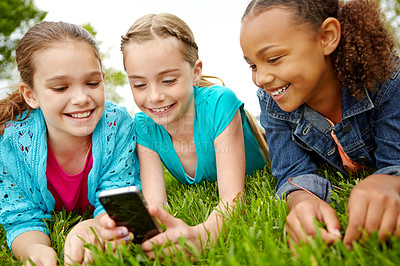 Buy stock photo Three little girls spending time together and sharing a smartphone while outdoors