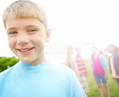 Buy stock photo Cute little boy smiling while standing outdoors with some friends in the background