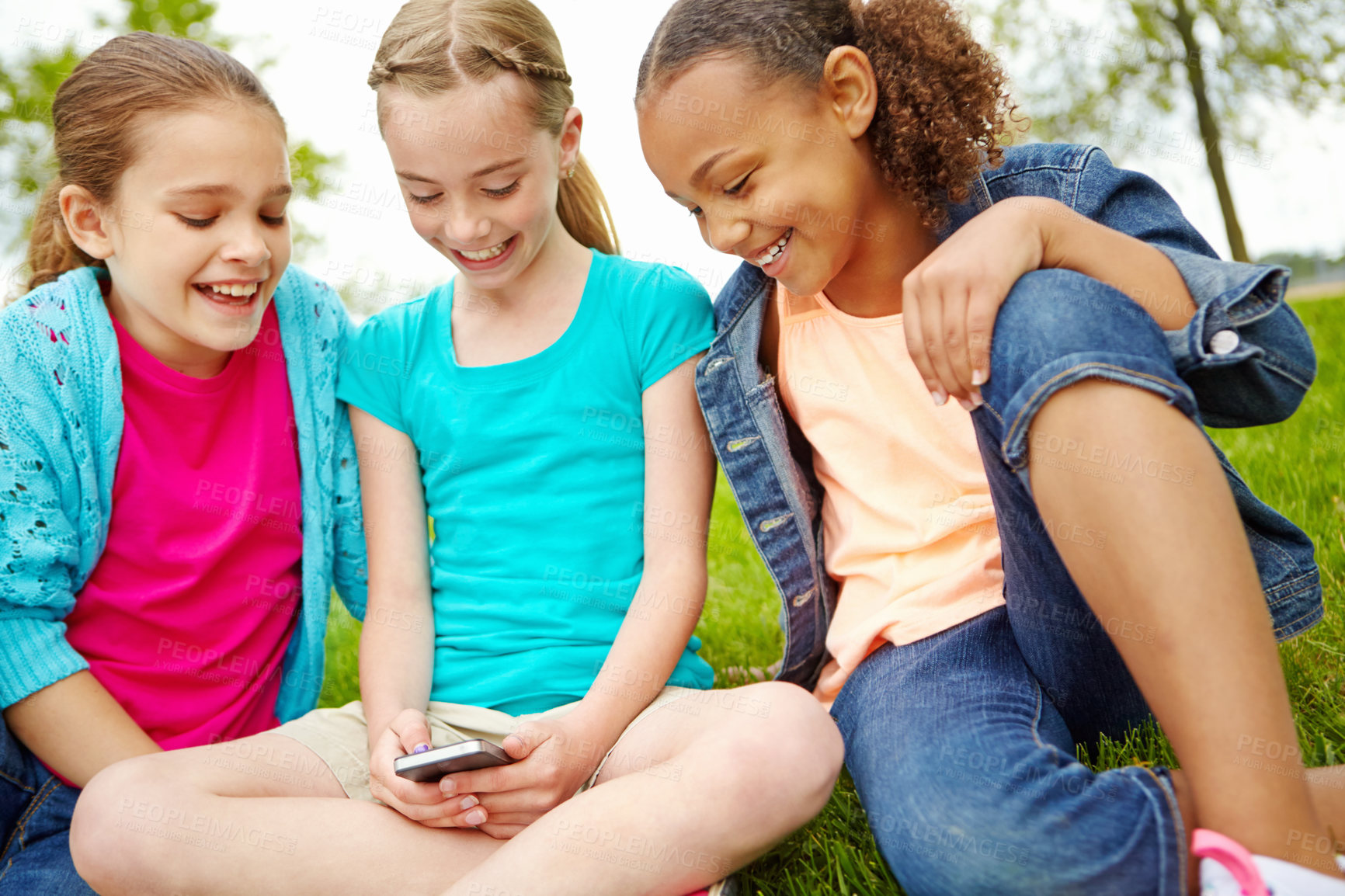 Buy stock photo Three little girls spending time together and sharing a smartphone while outdoors