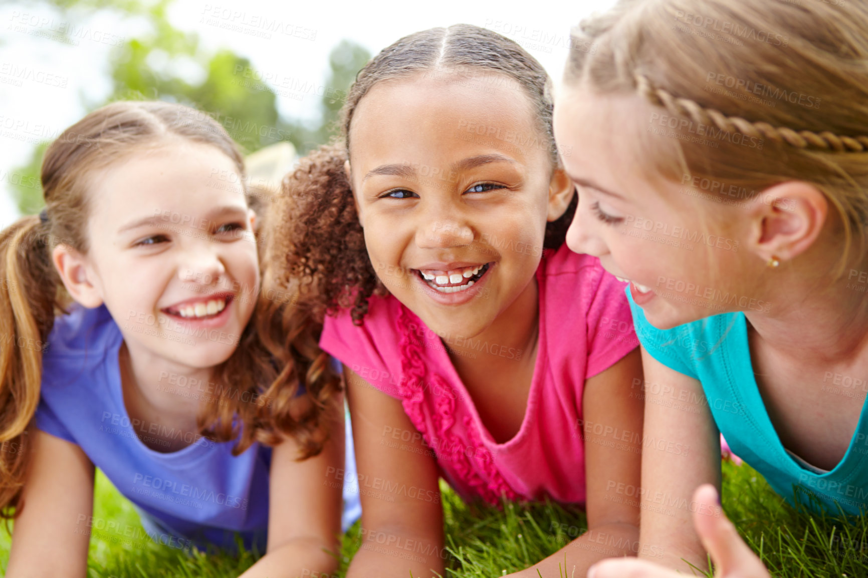 Buy stock photo Three multi-ethnic young girls lying on the grass in a park smiling at the camera