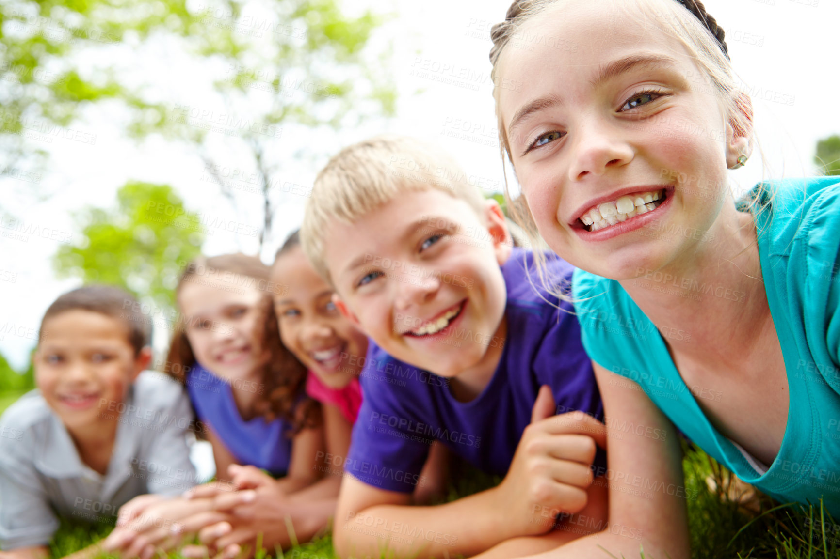 Buy stock photo A multi-ethnic group of children lying on the grass in a park smiling at the camera