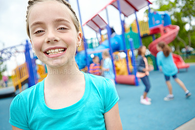 Buy stock photo A young girl smiling at the camera while her friends play behind her in a play park