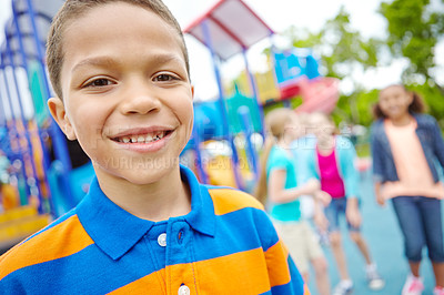 Buy stock photo A young African-American boy smiling at the camera while his friends play in a playground behind him