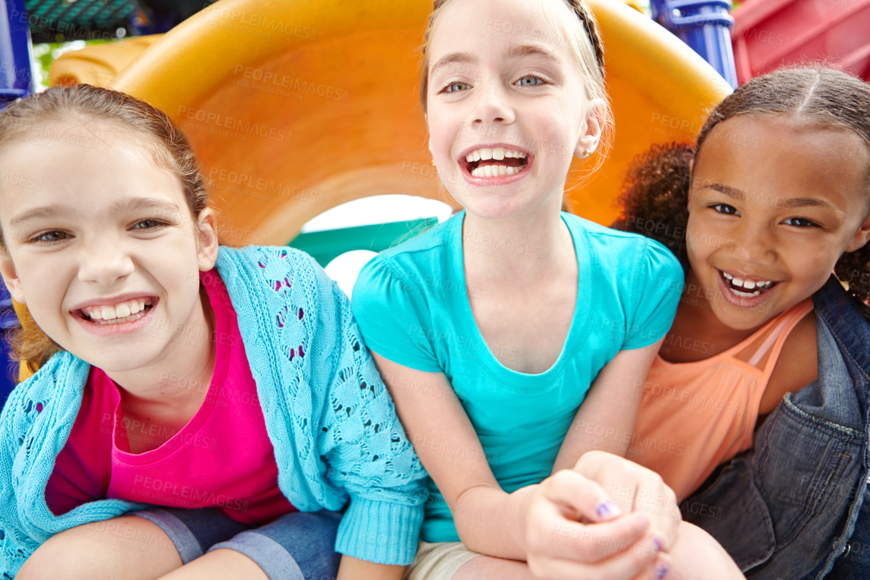 Buy stock photo Three happy young girls sitting on a slide in a playpark