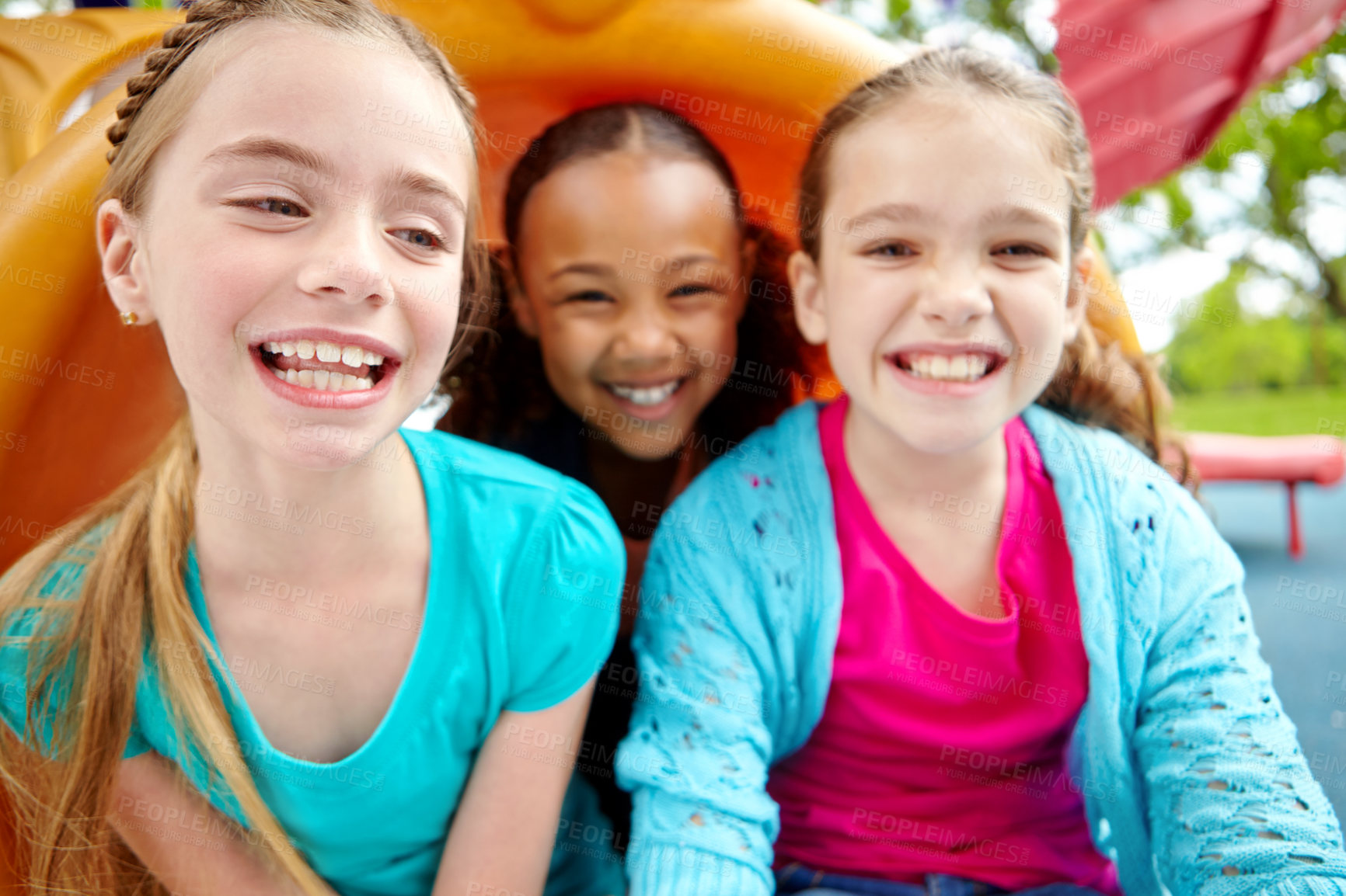 Buy stock photo Three happy young girls sitting on a slide in a playpark