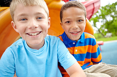 Buy stock photo Two happy young boys sitting on a slide in a play park