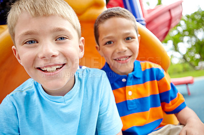 Buy stock photo Two happy young boys sitting on a slide in a play park