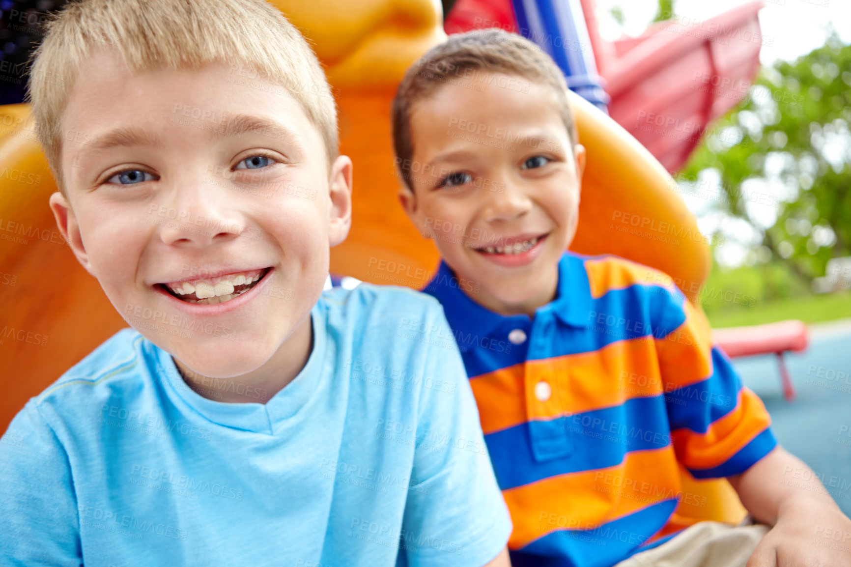 Buy stock photo Two happy young boys sitting on a slide in a play park