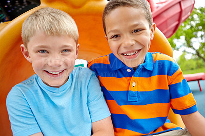 Buy stock photo Two happy young boys sitting on a slide in a play park