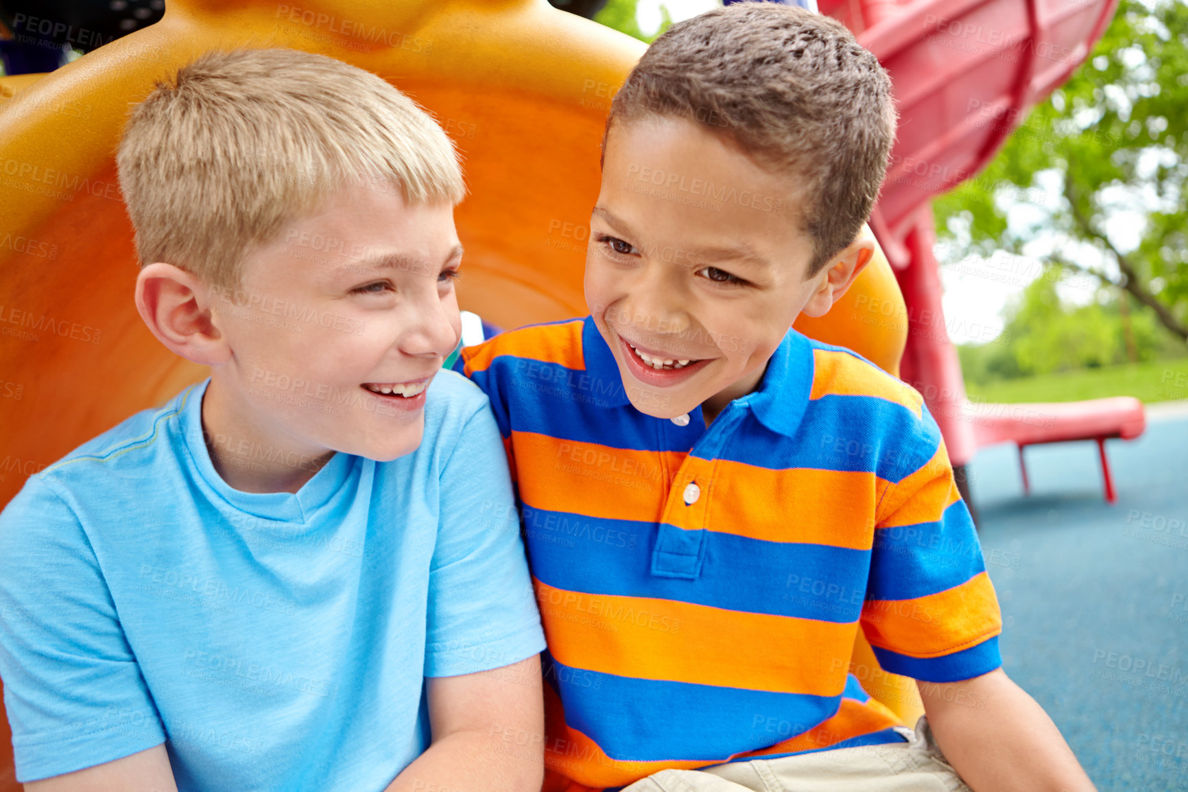 Buy stock photo Two happy young boys sitting on a slide in a play park