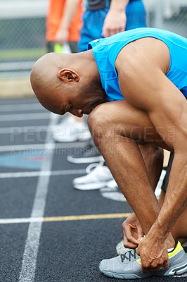 Buy stock photo Side view of a male athlete tying his shoelaces in preparation for the race