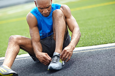 Buy stock photo Close up of a male athlete tying his shoelaces at the race track