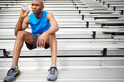 Buy stock photo Full length shot of a male athlete sitting on the rafters at the track and drinking water
