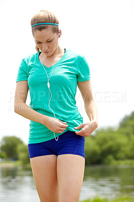 Buy stock photo Cropped shot of a female athlete standing outdoors and adjusting her MP3 player