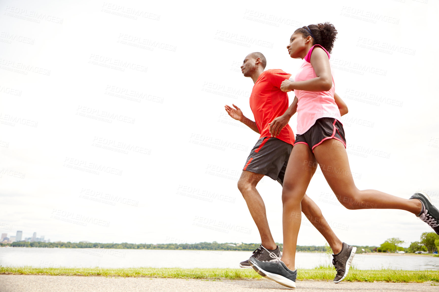Buy stock photo Full length side view of two athletes running next to a lake