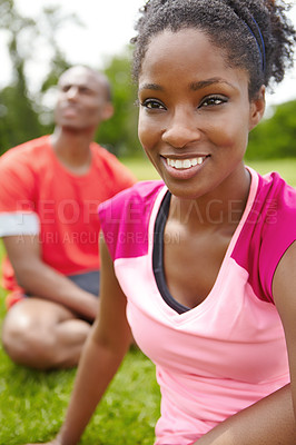 Buy stock photo Cropped close up of a female athlete sitting on the grass with a male athlete in the background
