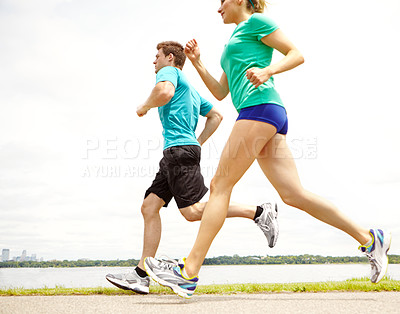 Buy stock photo Side view of two runners jogging next to a lake