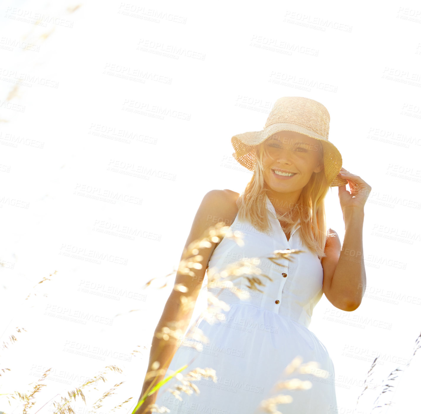 Buy stock photo A beautiful young blonde woman standing in a meadow wearing a sunhat on a summer's day