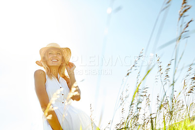 Buy stock photo A beautiful young blonde woman standing in a meadow wearing a sunhat on a summer's day