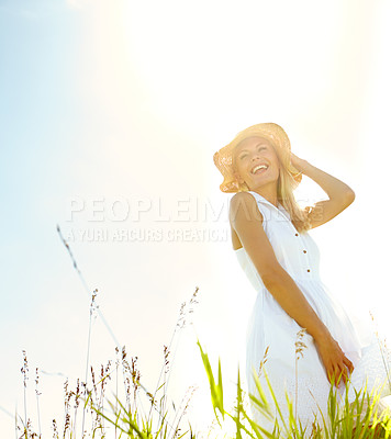 Buy stock photo A beautiful young blonde woman standing in a meadow wearing a sunhat on a warm summer's day