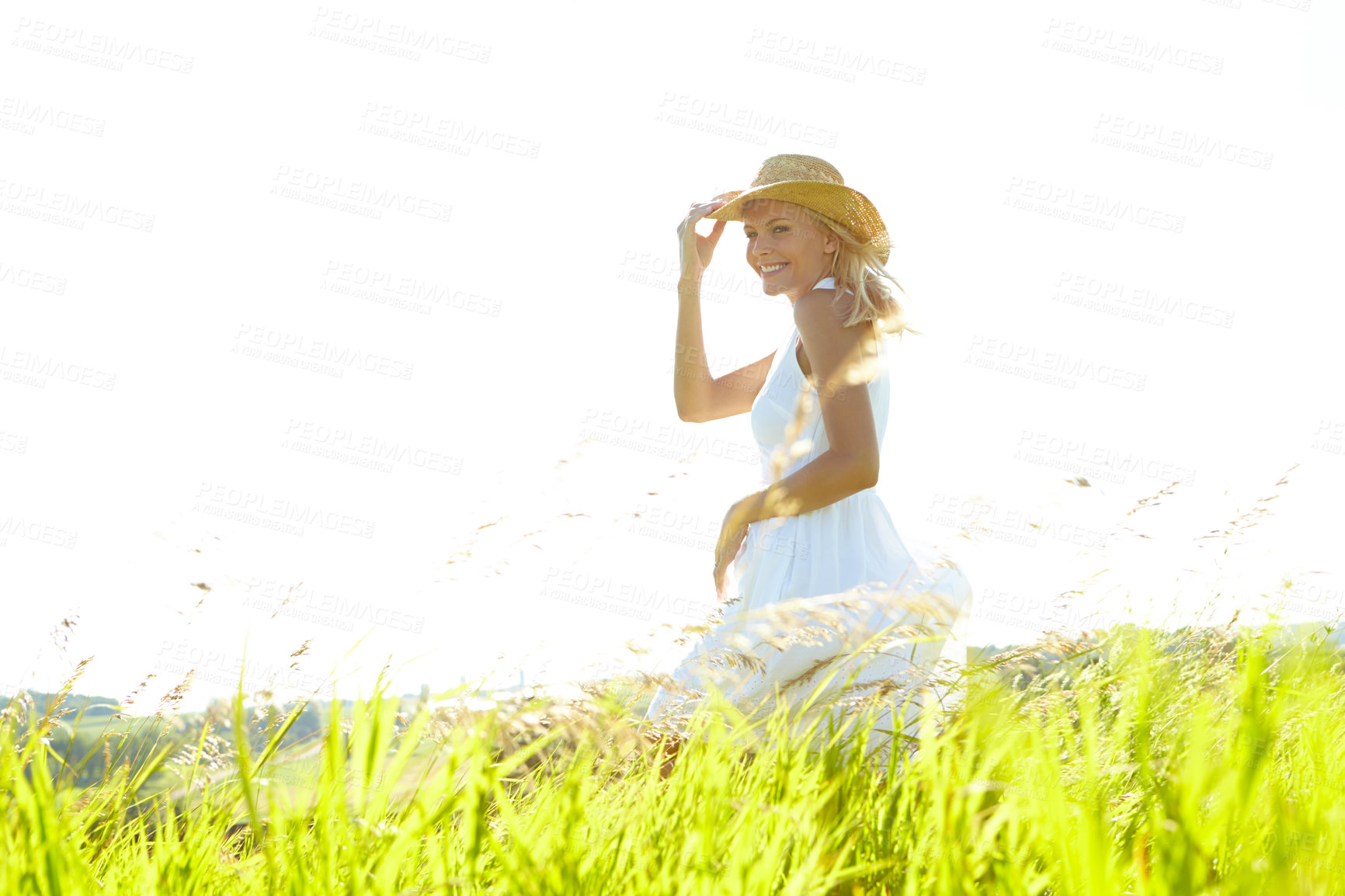 Buy stock photo A beautiful young blonde woman standing in a meadow wearing a sunhat on a warm summer's day